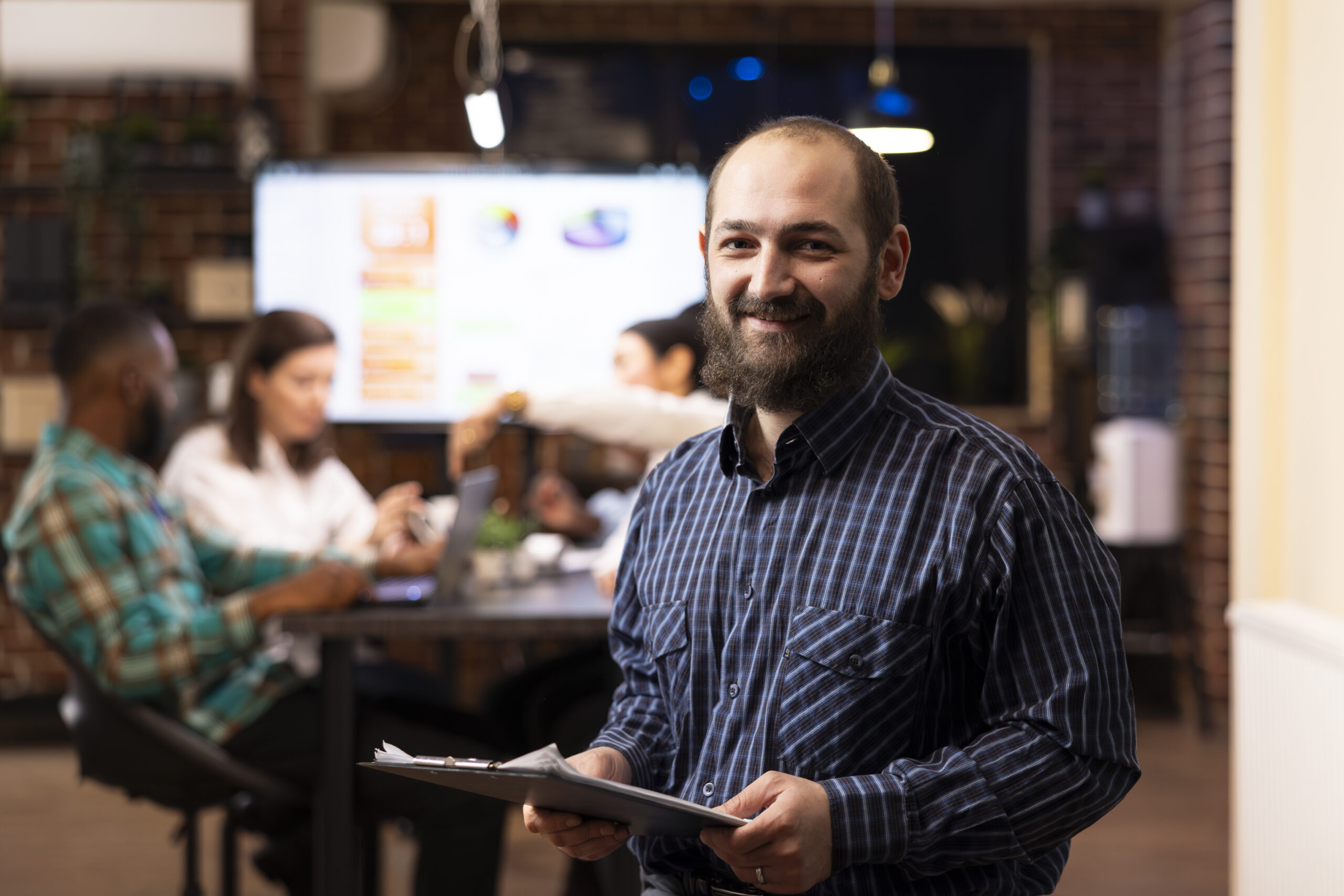 Determined businessman in checkered shirt ready to review project planning details in office. The modern workspace, late night teamwork and digital analytics highlight productivity.