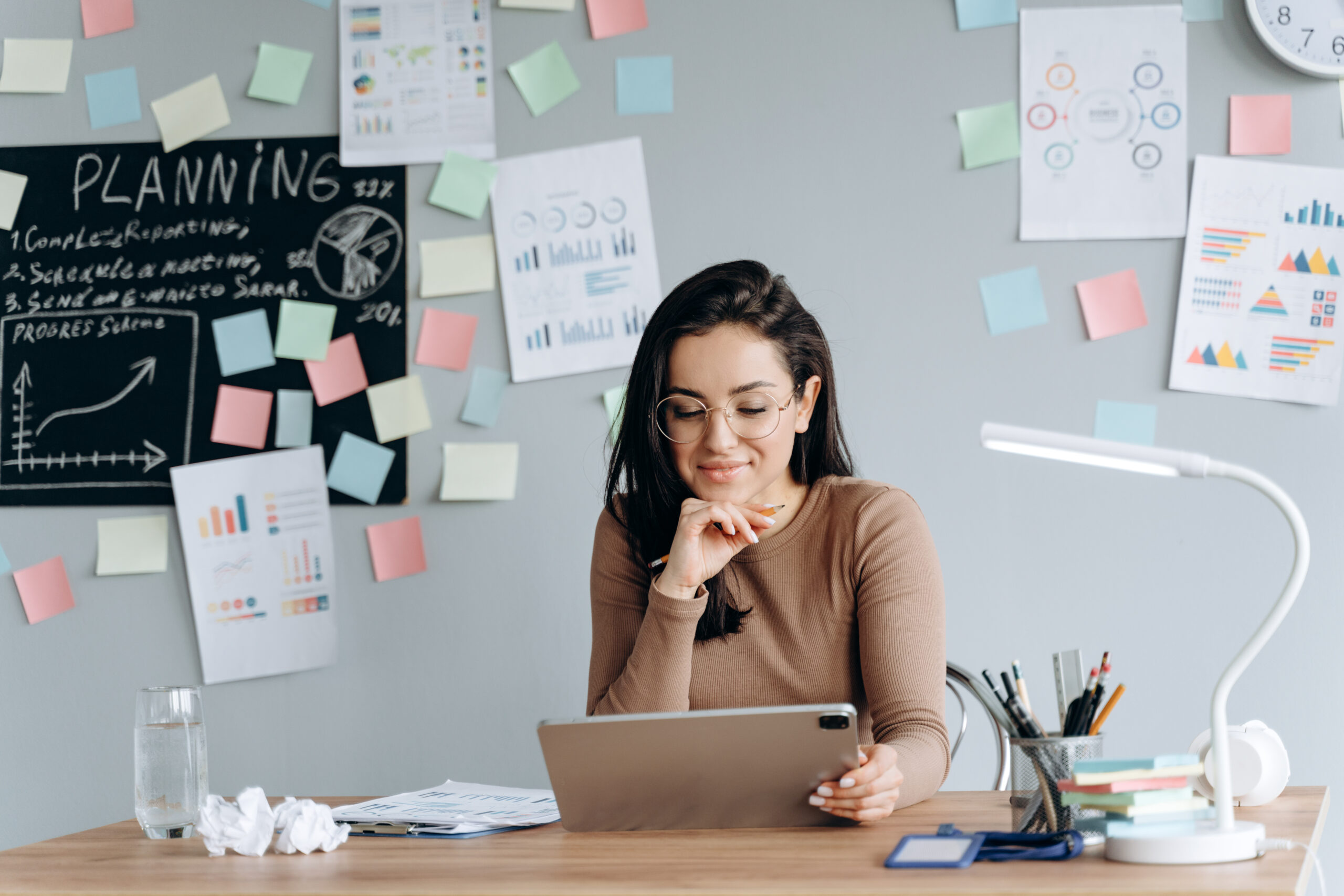 Charming brunette works at tablets, at the same time she makes important records in a gray cabinet. Employment concept.