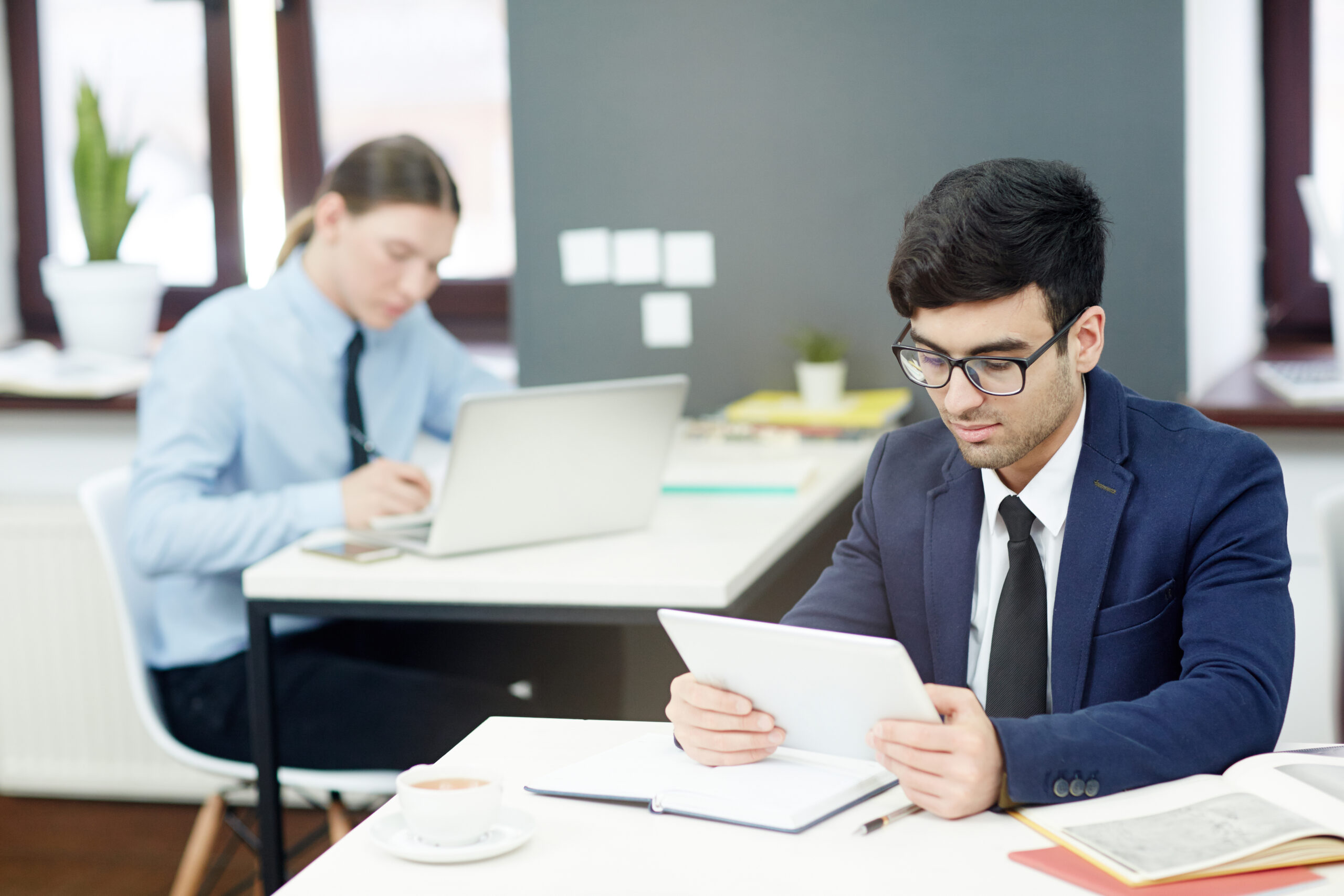 Concentrated young managers in formalwear preparing financial accounts on computers while sitting at modern open plan office