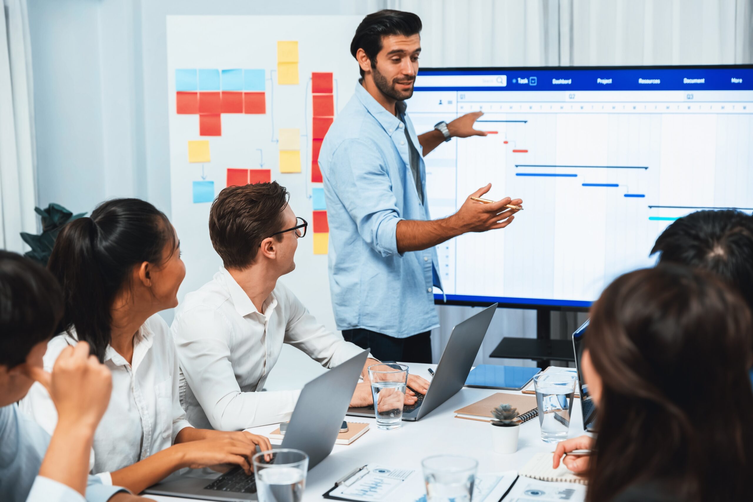 Project manager communicate and collaborate with team using project management software display on monitor, tracking progress of project task and making schedule plan at meeting table. Prudent